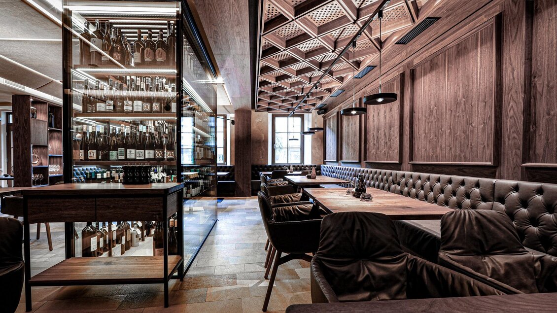 Ein elegantes Restaurant mit Holzverkleidung und gedämpfter Beleuchtung. Die Einrichtung umfasst gemütliche Sitzgelegenheiten und eine eindrucksvolle Bar mit Weinregalen. | © Alte Post Südsteiermark