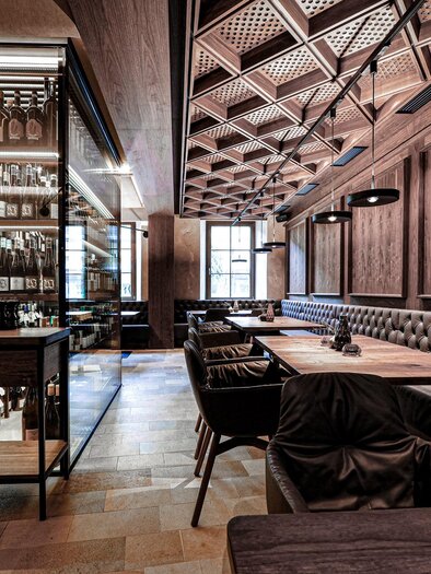 An elegant restaurant with wooden paneling and subdued lighting. The decor includes cozy seating and an impressive bar with wine racks. | © Alte Post Südsteiermark