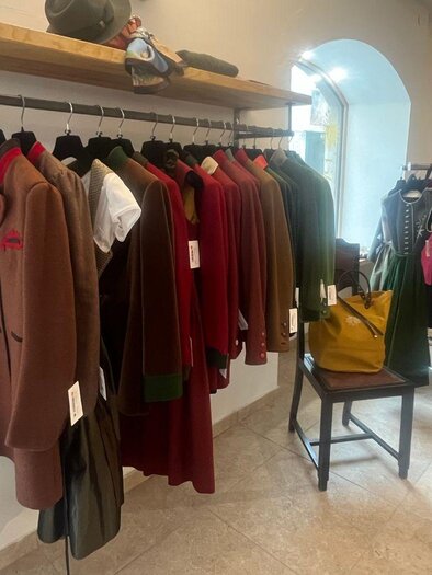 Ein Verkaufsraum mit traditionellen Kleidungsstücken an Kleiderständern. Die Kleidung ist hauptsächlich in rustikalen Farbtönen gehalten, und es gibt einige Accessoires auf einem Tisch. | © TVB Ausseerland Salzkammergut_Nathalie Schröttenhamer