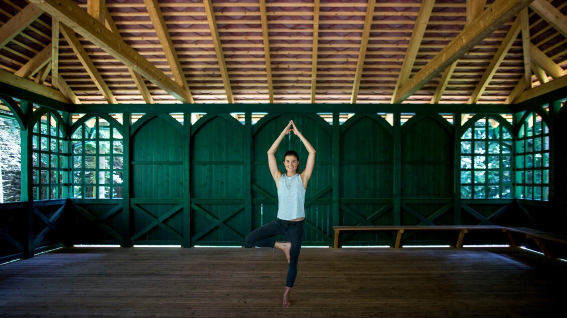Eine Frau praktiziert Yoga im geschlossenen Holzpavillon des Arboretums Laßnitzhöhe. | © Region Graz - Tom Lamm
