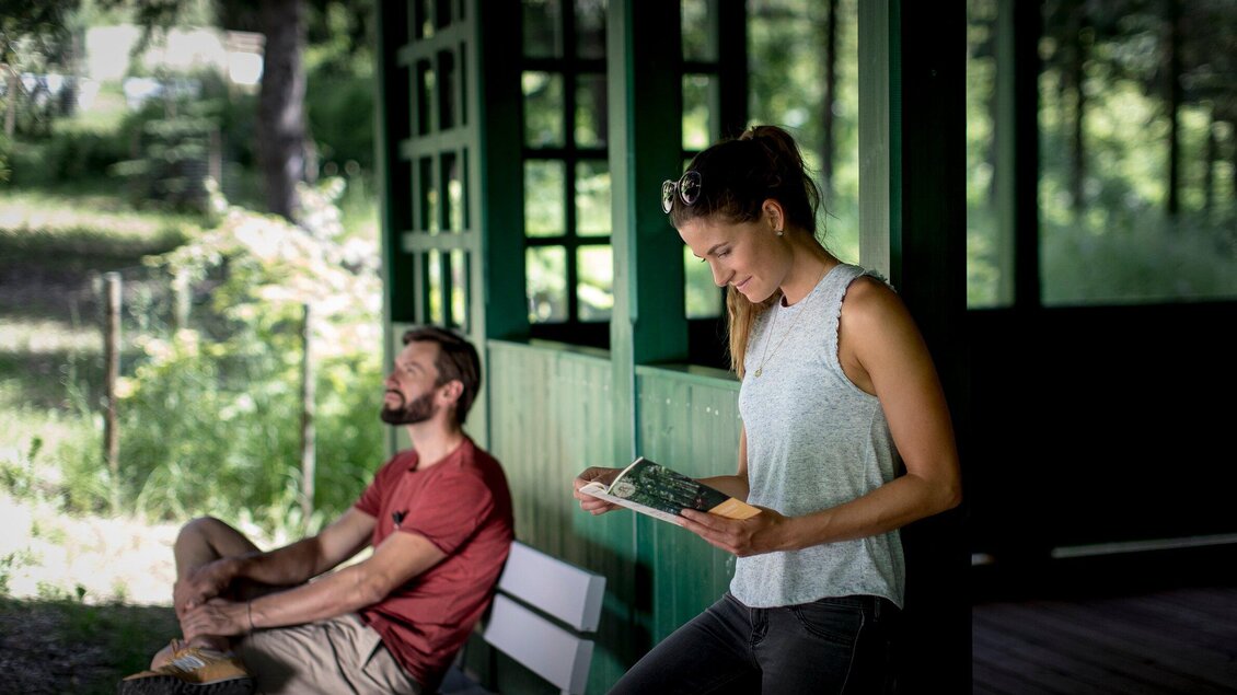 Eine Frau liest, während der Mann sich im Schatten des Aboretum Laßnitzhöhe auf einer Bank erholt. | © Region Graz - Tom Lamm