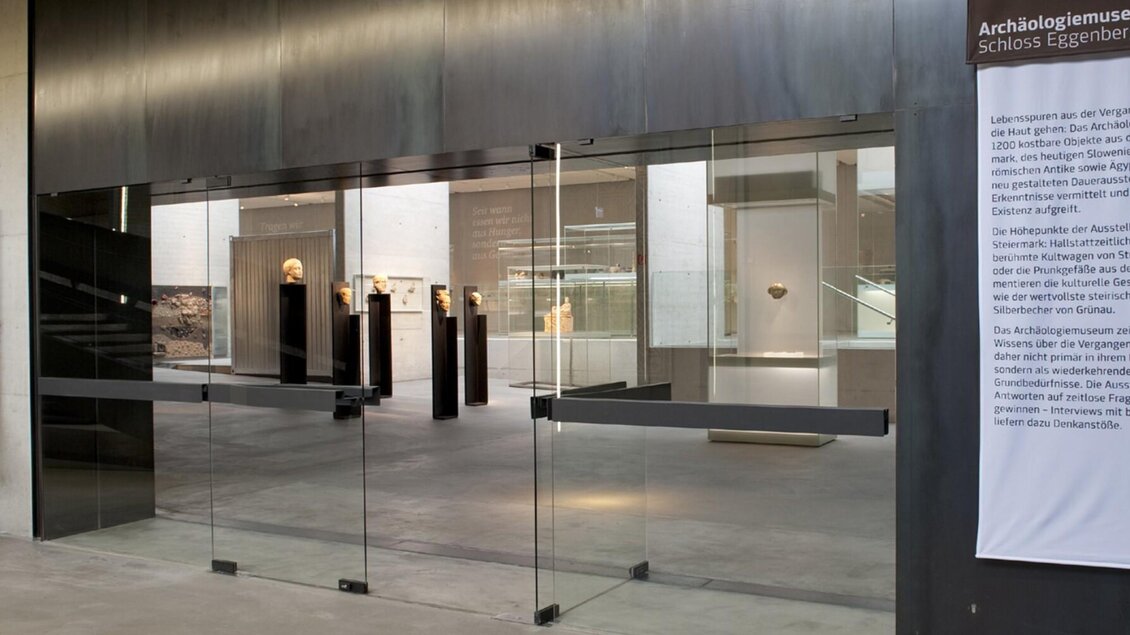 Der moderne Eingang des Archäologiemuseums im Schloss Eggenberg in Graz, mit Blick auf Ausstellungsstücke und eine informative Wand. | © UMJ-N. Lackner