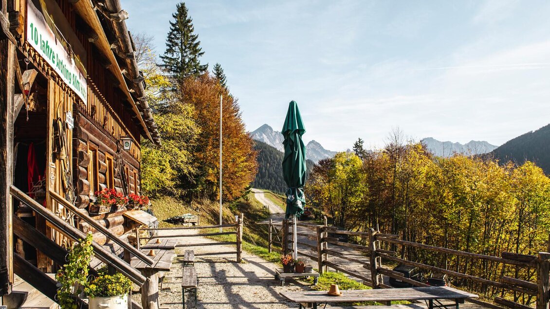 Eine gemütliche Berghütte umgeben von buntem Herbstlaub. Im Hintergrund sind die Berge und ein klarer Himmel zu sehen. | © Stefan Leitner
