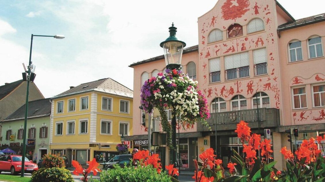 Ein charmantes Stadtbild mit bunten Blumen und historischen Gebäuden. Die Straße ist belebt und zeigt typische Architektur. | © Robert Cescutti