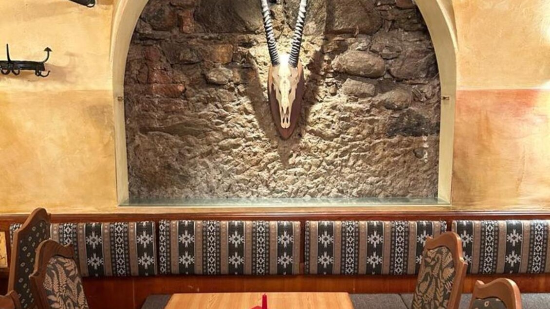 Ein gemütliches Restaurant mit holzverkleideten Wänden und dekorativen Elementen. Im Hintergrund hängt ein Geweih an der Wand, während ein Tisch für Gäste gedeckt ist. | © Arkadenhof