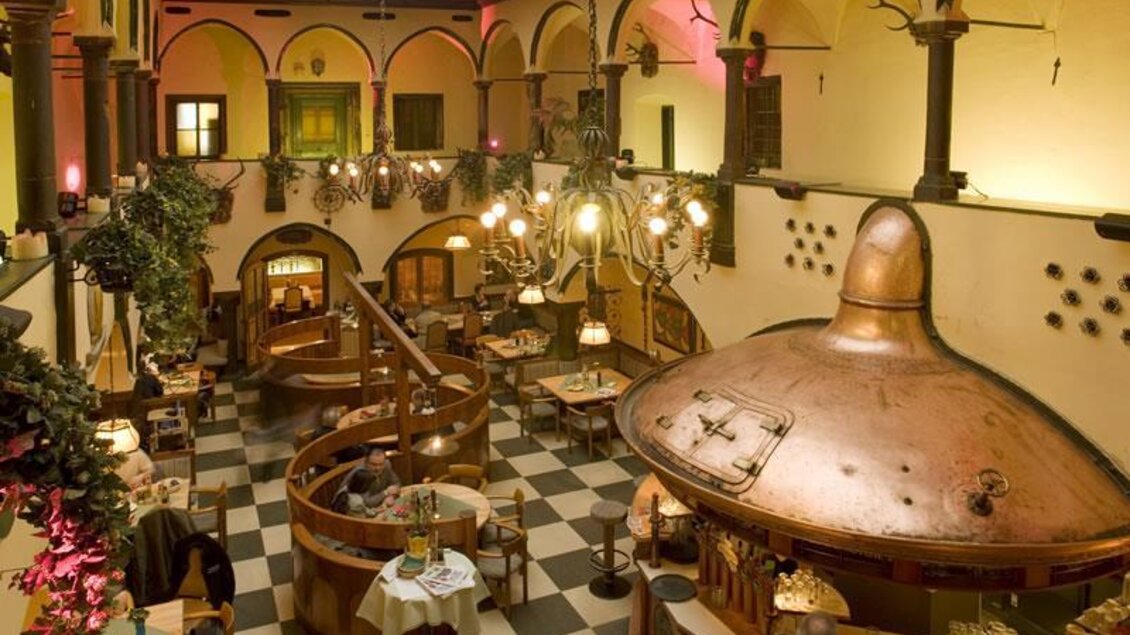 Ein gemütliches Restaurant mit Holzdekor und runden Tischen. Im Mittelpunkt steht ein großer Kupferkessel. | © Arkadenhof