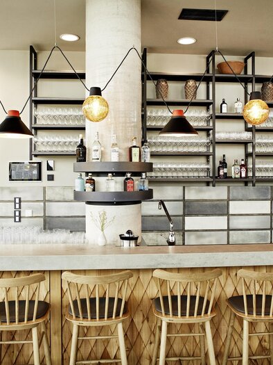 A modern bar with wooden chairs and an elegant counter. In the background, shelves with glasses and drinks are visible. | © Arravané - Gerhard Wasserbauer
