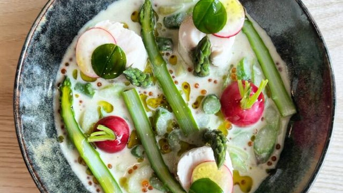 Ein elegantes Gericht in einer Schale, angerichtet mit Spargel, Radieschen und einem cremigen, hellen Dressing. Frische Kräuter und essbare Blüten sorgen für einen farbenfrohen Akzent. | © Arravané
