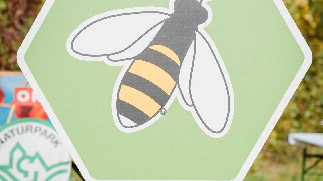 Ein sechseckiges Schild mit einer abgebildeten Biene in der Mitte. Der Text "Bee Wild" fordert dazu auf, Patenschaft für den Artenschutz zu übernehmen. | © Bee Wild