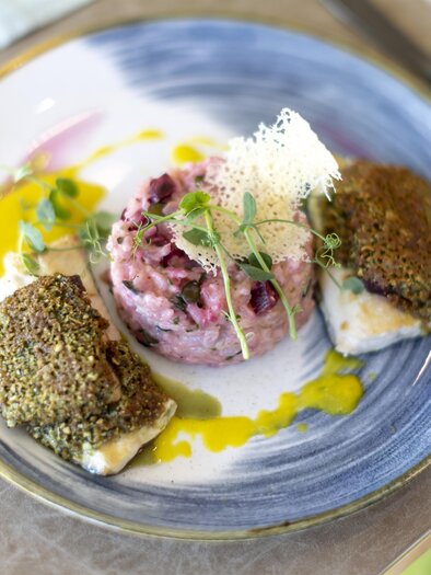 An elegant plate with fried fish and a pink risotto.  
Garnished with fresh herbs and a fine sauce. | © TVB Thermen- & Vulkanland