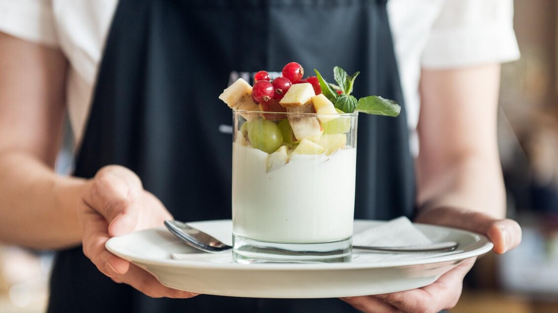 Glass with yogurt and fresh fruits, served on a plate with spoon. | © Martin Auer