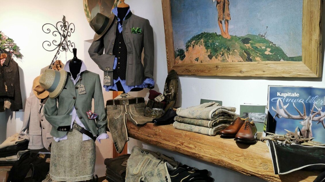 Ein gemütlicher Bekleidungsladen mit traditionellen Kleidungsstücken, darunter Jacken und Hosen. Es gibt auch stilvolle Schuhe und eine wunderschöne Wandmalerei im Hintergrund. | © Alexander Greul