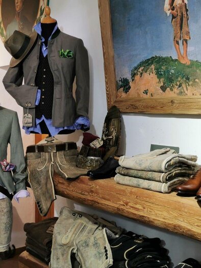 Ein gemütlicher Bekleidungsladen mit traditionellen Kleidungsstücken, darunter Jacken und Hosen. Es gibt auch stilvolle Schuhe und eine wunderschöne Wandmalerei im Hintergrund. | © Alexander Greul