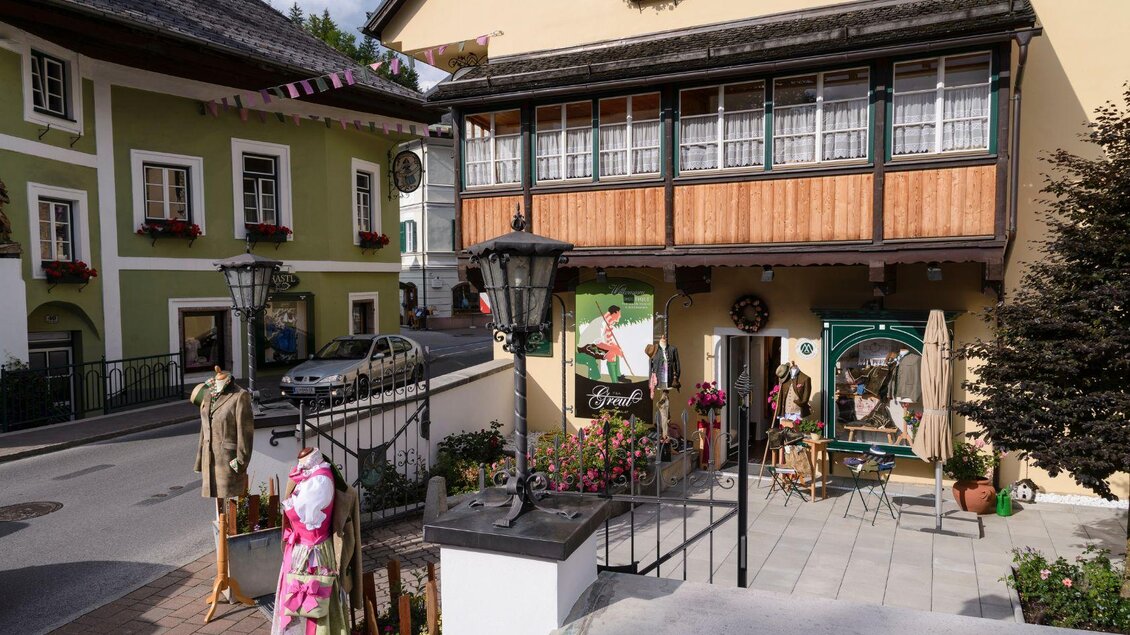 Eine charmante Straßenansicht mit einem traditionellen Gebäude und Fenstern mit Blumen. Vor dem Haus stehen Schaufensterpuppen in ansprechender Kleidung. | © Alexander Greul