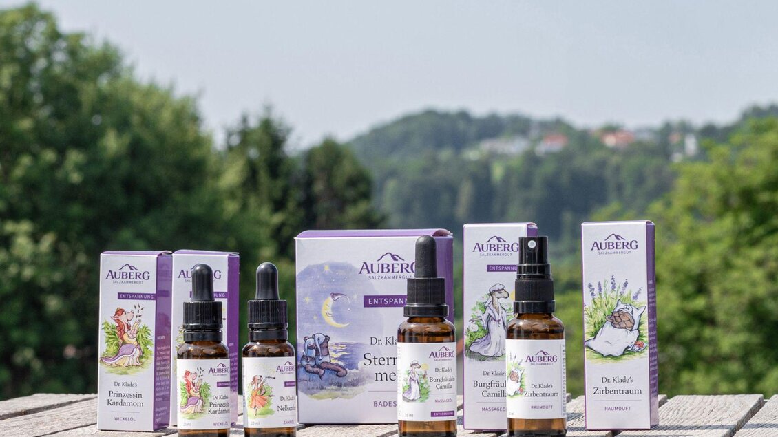 Eine Auswahl von Naturheilmitteln in Fläschchen, auf einem Holztisch platziert. Im Hintergrund ist eine grüne Landschaft mit Bäumen und Hügeln zu sehen. | © Caroline Klade