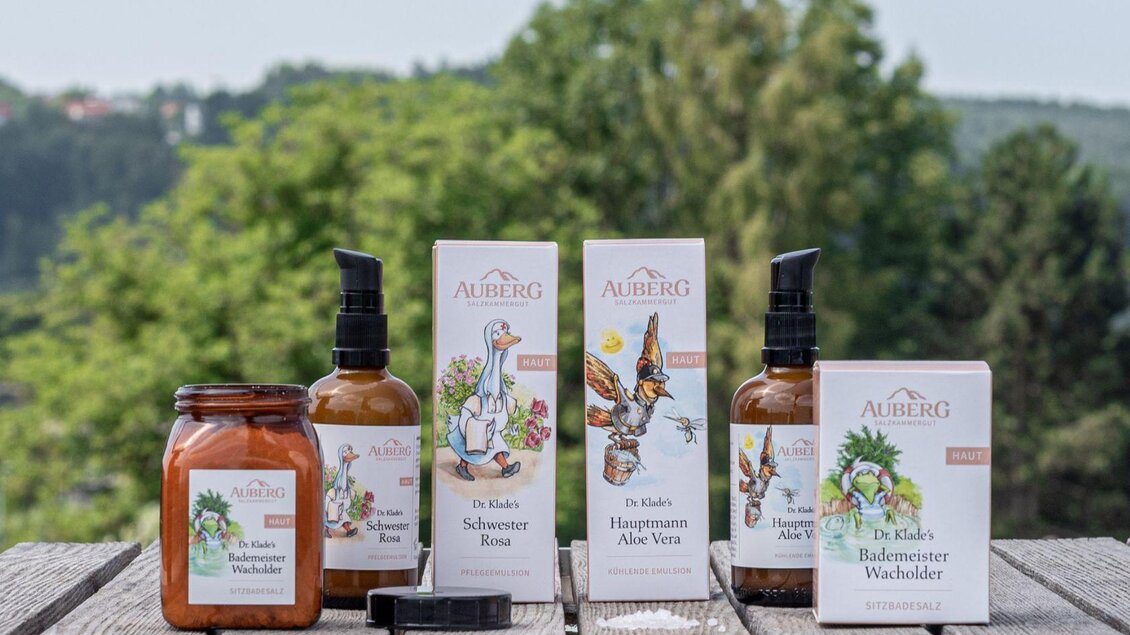 Eine Auswahl von Hautpflegeprodukten steht auf einem Holztisch. Im Hintergrund sieht man eine grüne Landschaft mit Bäumen. | © Caroline Klade