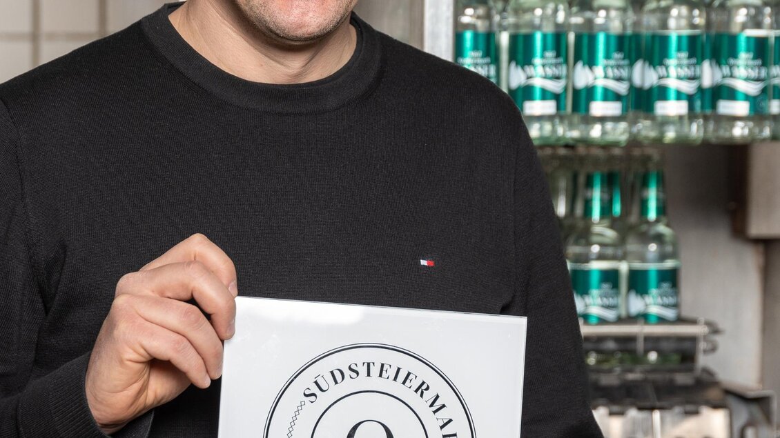 Ein lächelnder Mann hält ein Zertifikat in der Hand. Im Hintergrund sind Maschinen und Ausrüstung zu sehen. | © RM SW GmbH | webquartier.at