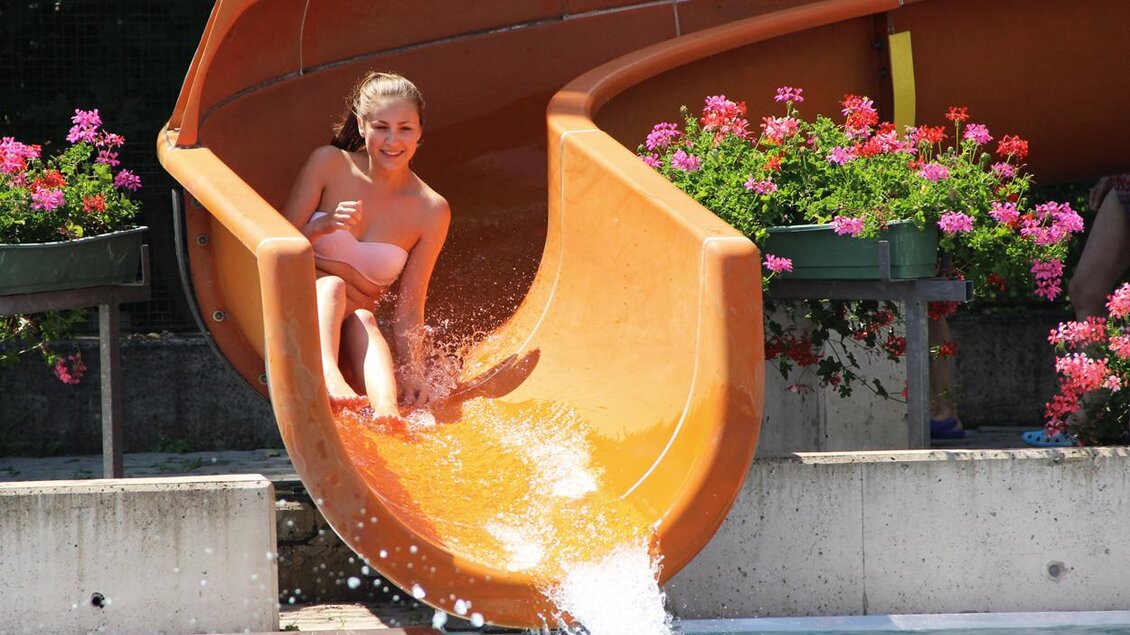 Junge Frau rutscht auf orangener Wasserrutsche ins Becken des Augartenbads Graz | © Holding Graz-Enrico Radaelli