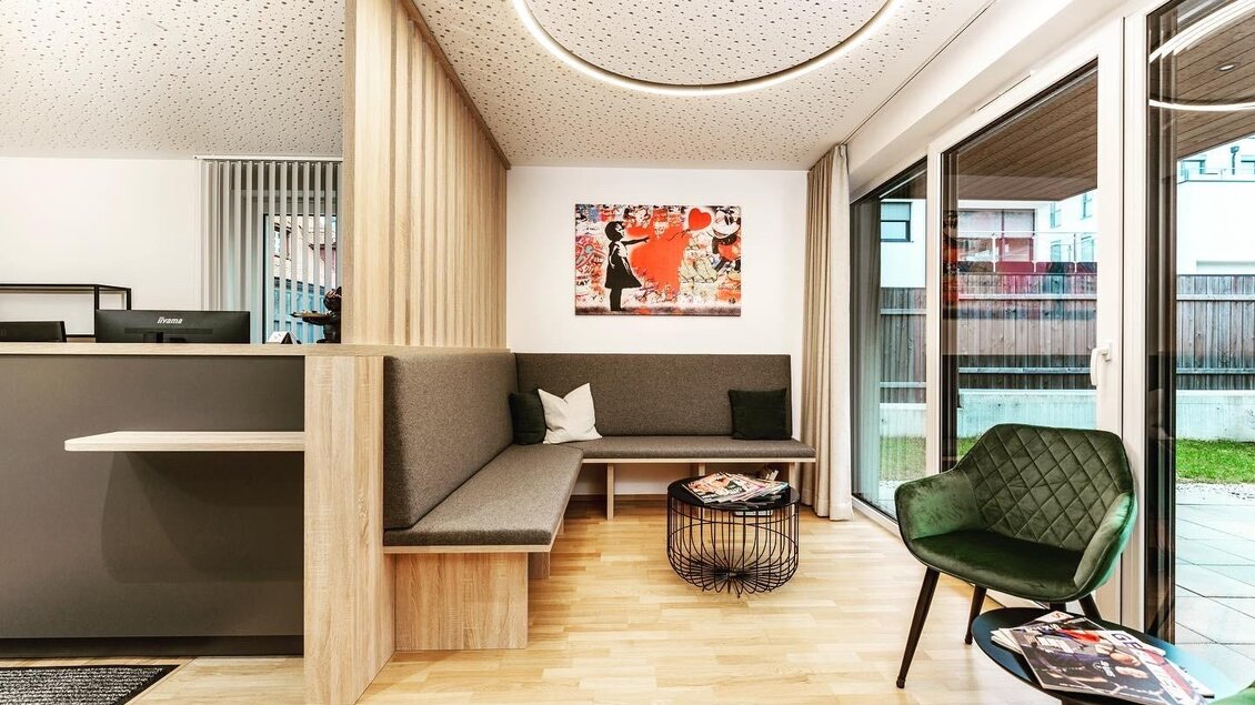 Ein modernes Empfangsbereich mit elegantem Mobiliar. Der Raum hat große Fenster, die viel Licht hereinlassen, und eine künstlerische Wandgestaltung.