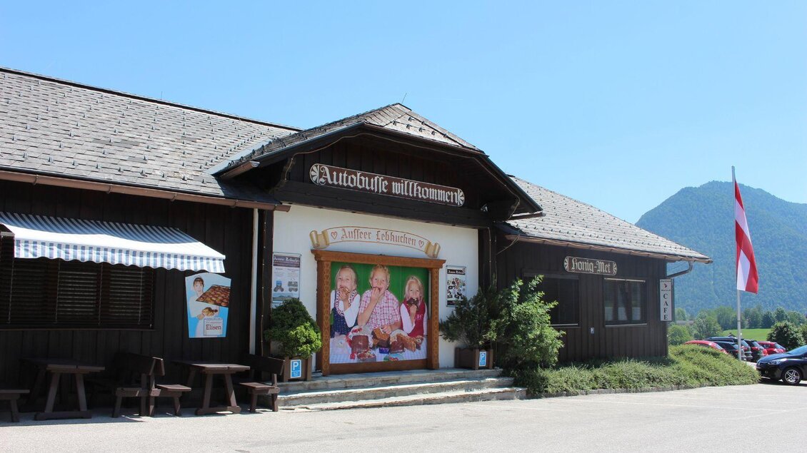 Ein traditionelles Gasthaus mit Holzfassade und einem großen Wandbild. Im Vordergrund befinden sich Sitzmöglichkeiten und eine schöne Berglandschaft im Hintergrund. | © TVB Ausseerland Salzkammergut/Viola Lechner