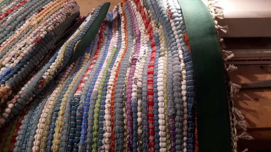 Ein buntes gewebtes Teppichstück mit verschiedenen Farben und Mustern. Das Material ist aus kleinen, runden Elementen gefertigt und hat einen grünen Rand. | © Ausseer Teppich