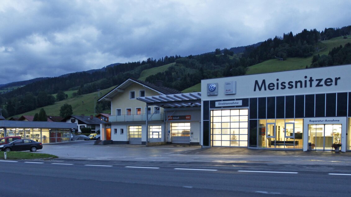 Ein Autohaus mit dem Namen "Meissnitzer" liegt an einer Straße. Im Hintergrund sind hügelige Landschaften und ein bewölkter Himmel zu sehen. | © Autohaus Meissnitzer