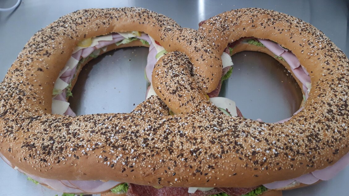 Ein großes Sandwich in Form einer Brezel, gefüllt mit Schinken und Käse. Es ist mit Sesam und Mohn bestreut. | © Bäckerei Posch