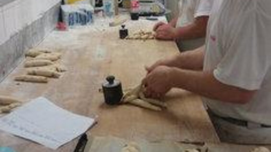 Zwei Bäcker formen Teig auf einer Arbeitsfläche. Im Hintergrund sind verschiedene Utensilien und Zutaten zu sehen. | © Bäckerei Posch