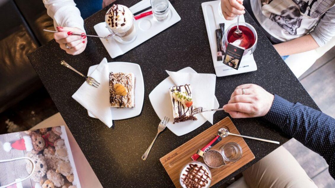 Ein Tisch mit verschiedenen Desserts, darunter Kuchen und Eis, ist gedeckt. Personen genießen ihre Leckereien und Getränke in einer gemütlichen Umgebung. | © Bäckerei Birchbauer