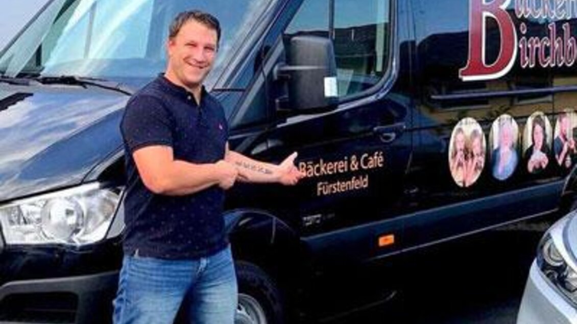Ein Mann steht neben einem schwarzen Lieferwagen mit der Aufschrift „Bäckerei & Café Fürstenfeld“. Er zeigt stolz auf den Van. | © Bäckerei Birchbauer