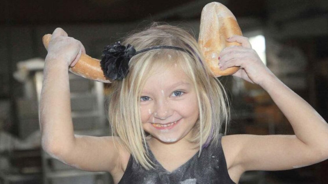 Ein lachendes Mädchen hält zwei Brote wie Hörner über dem Kopf. Sie ist in einer Bäckerei und hat Mehl auf ihrem Gesicht. | © Bäckerei Birchbauer
