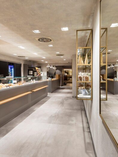 Ein modernes Café oder Bäckerei mit hellen Wänden und eleganten Regalen. Überall sind frisch gebackene Brötchen und Croissants zu sehen. | © Sorger - Werner Krug