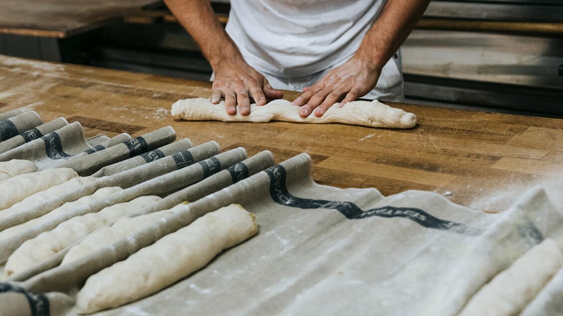 Bäcker formt Brotlaibe von Hand auf Holzfläche in der Backstube | © Sorger - Lupi Spuma
