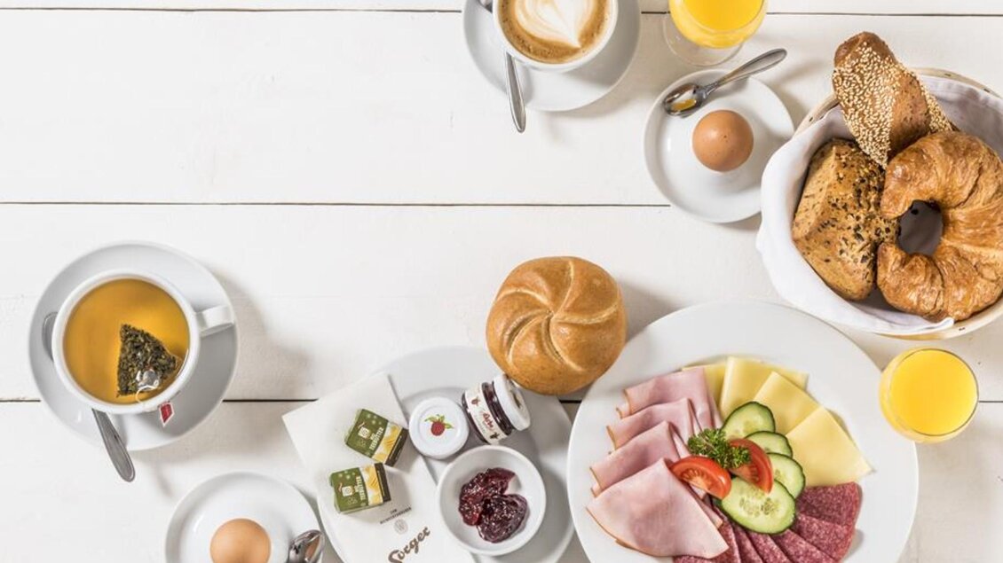 Ein reichhaltiges Frühstück mit Wurst, Käse, frischen Brötchen und Obst. Dazu gibt es Tee, Kaffee und Säfte auf einem hellen Tisch. | © Werner Krug