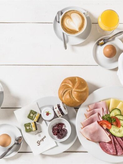 Ein reichhaltiges Frühstück mit Wurst, Käse, frischen Brötchen und Obst. Dazu gibt es Tee, Kaffee und Säfte auf einem hellen Tisch. | © Werner Krug