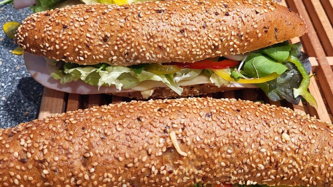 Vier belegte Sesambrötchen mit frischem Gemüse liegen auf einem Holzbrett. Die Brötchen sind gut gefüllt und appetitlich angerichtet. | © Tourismusverband Oststeiermark