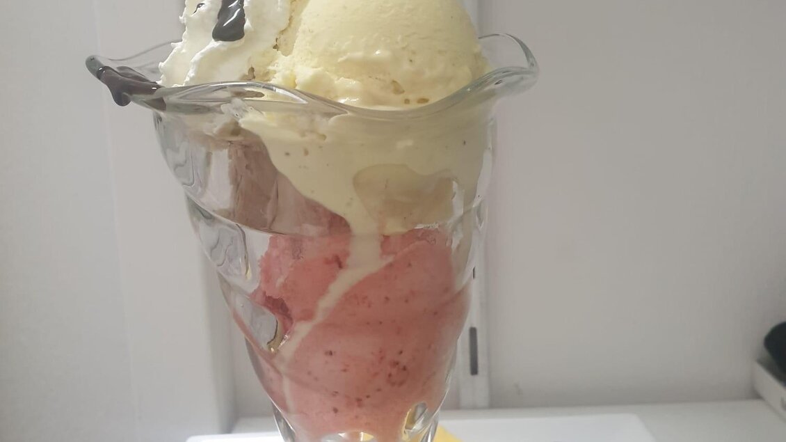 Ein köstliches Eisbecher mit verschiedenen Eissorten, Sahne und einer Waffel. Neben dem Glas liegt ein Löffel und eine gelbe Serviette. | © Tourismusverband Oststeiermark