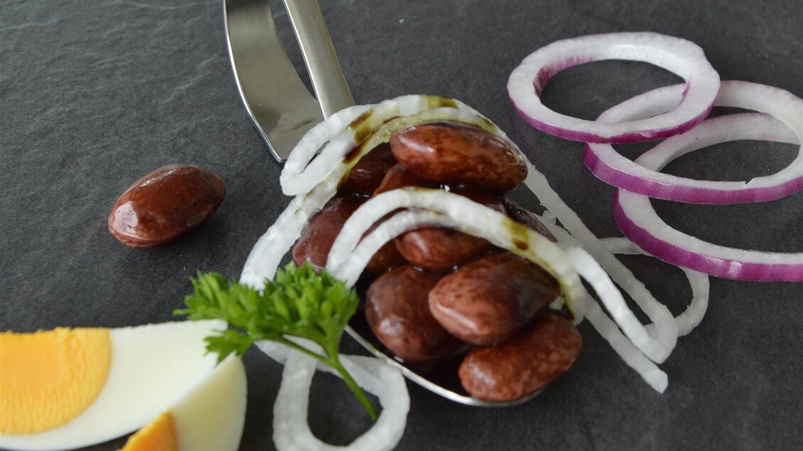 Ein Löffel mit roten Bohnen, garniert mit Zwiebelringen und frischem Koriander. Neben dem Löffel liegen Eier und weitere Zwiebelringe auf einer Steinplatte. | © Bäcksteffl