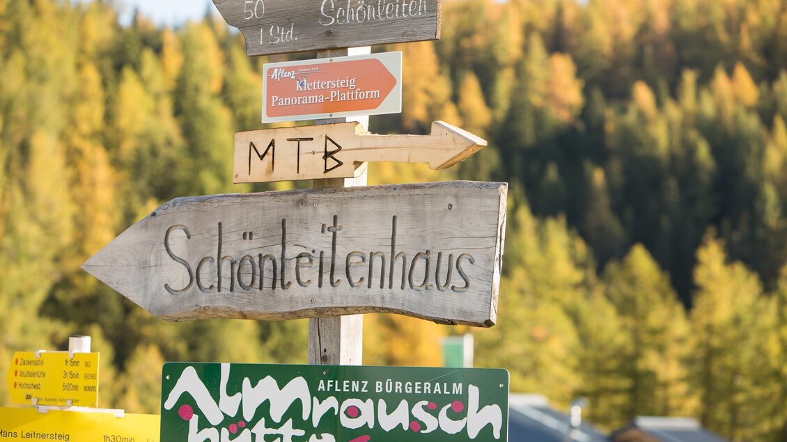 Ein Schild mit verschiedenen Wegweisungen in der Natur. Die Richtung zeigt zu "Schönteilenhaus" und "Almrauschhütte".