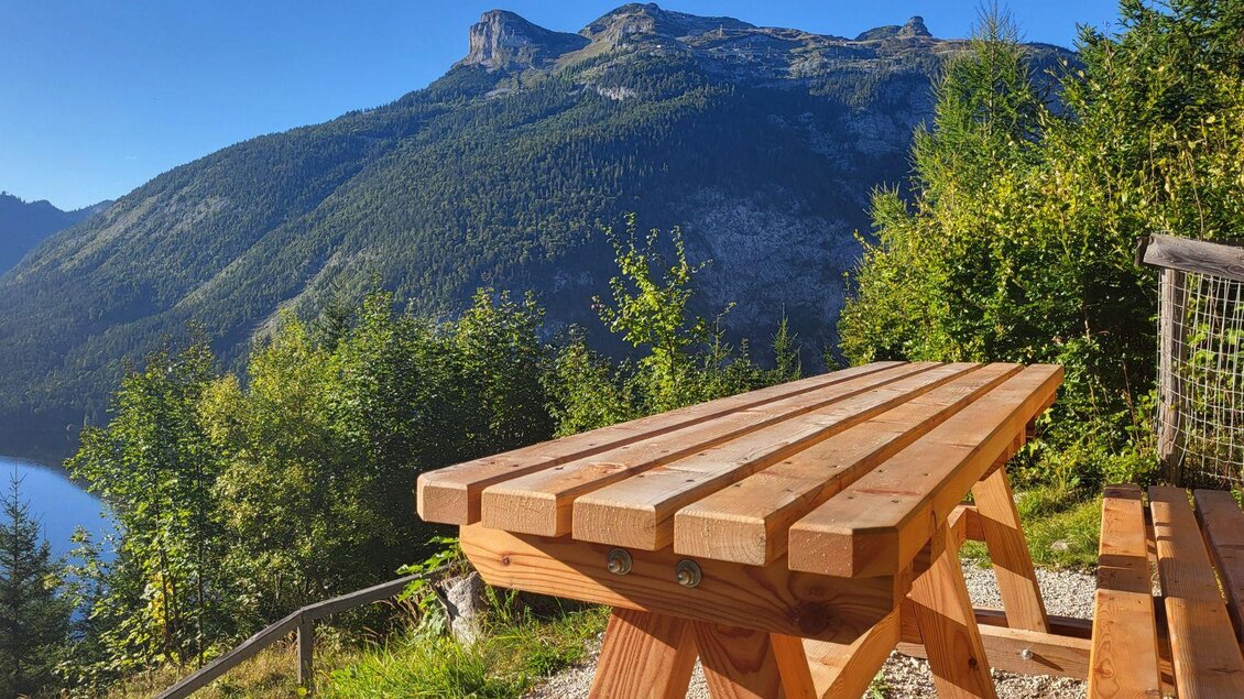 Eine Holzbank mit Blick auf eine beeindruckende Berglandschaft. Im Hintergrund sind grüne Bäume und ein klarer blauer Himmel zu sehen. | © TVB Ausseerland Salzkammergut_Petra Kirchschlager