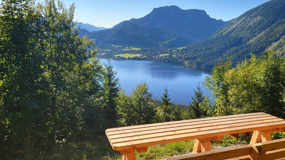 Eine malerische Aussicht auf einen klaren See, umgeben von Bergen und Wäldern. Im Vordergrund steht eine Holzbank, die zum Verweilen einlädt. | © TVB Ausseerland Salzkammergut_Petra Kirchschlager