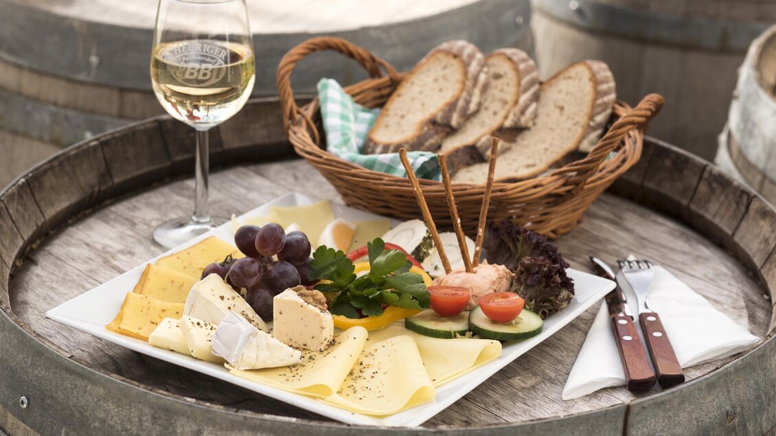 Ein rustikales Käsebrett mit einer Auswahl an Käsesorten, Trauben und frischem Gemüse. Dazu ein Glas Weißwein und ein Korb mit frischem Brot. | © Bernhard Bergmann