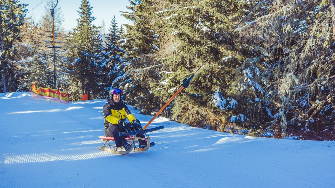 Eine Person sitzt auf einem Schlitten inmitten eines schneebedeckten Waldgebiets. Die Sonne scheint und die Bäume sind mit Schnee bedeckt. | © Tourismusverband Murau