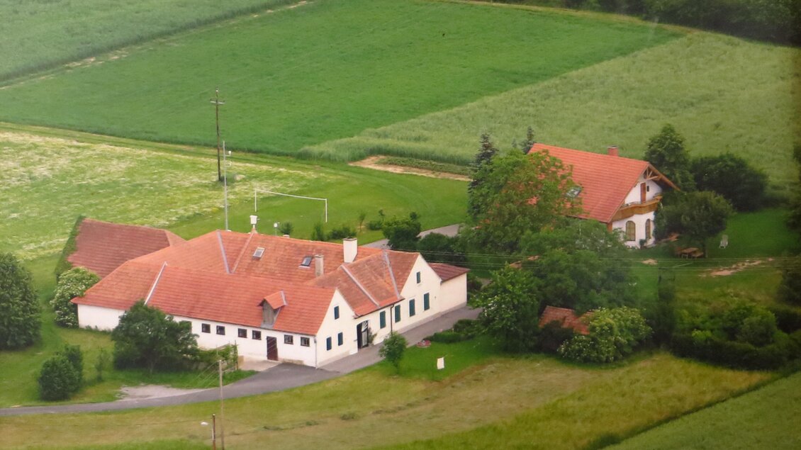 Ein landwirtschaftliches Anwesen mit rot gedecktem Hauptgebäude und einem danebenstehenden Haus. Umgeben von grünen Wiesen und Feldern. | © BIO HOF Rauscher