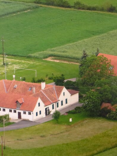 Ein landwirtschaftliches Anwesen mit rot gedecktem Hauptgebäude und einem danebenstehenden Haus. Umgeben von grünen Wiesen und Feldern. | © BIO HOF Rauscher