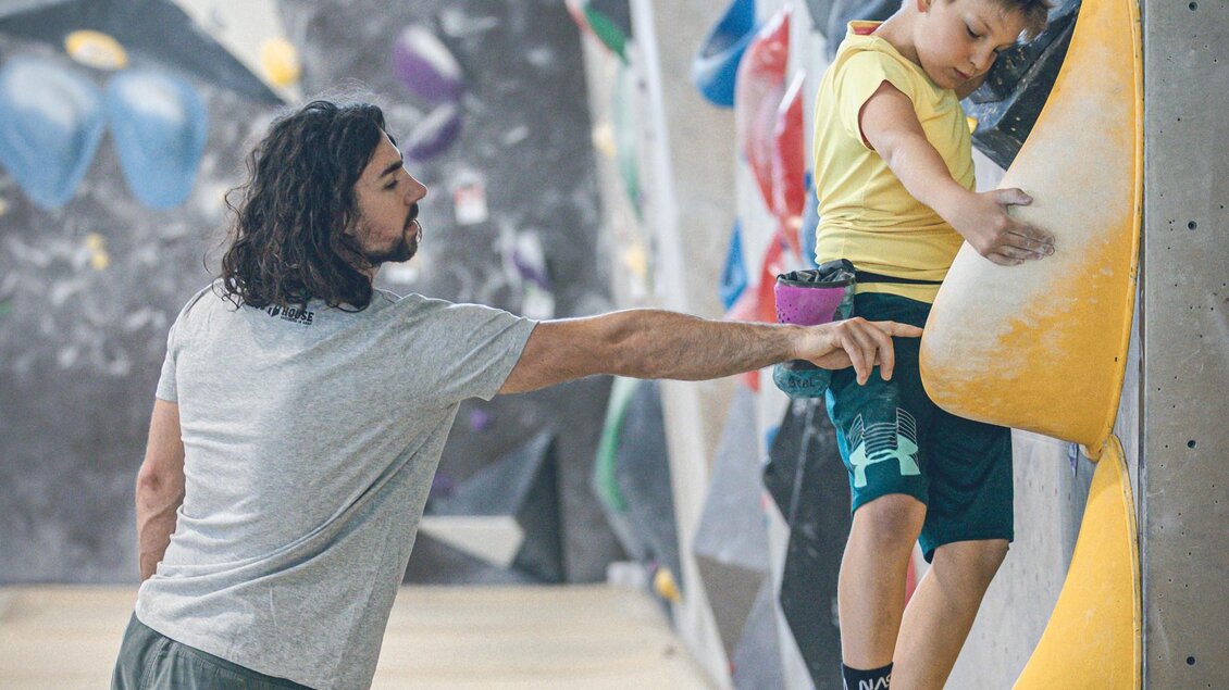 Trainer unterstützt Kind beim Bouldern an gelbem Griff im BLOC HOUSE Graz | © by AchimR