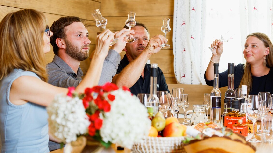 Eine Gruppe von vier Personen hebt Gläser zu einem Toast in einem gemütlichen Raum. Auf dem Tisch sind Getränke und frische Früchte arrangiert. | © Obsthof Brandl