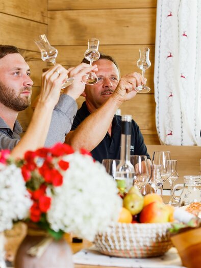 Eine Gruppe von vier Personen hebt Gläser zu einem Toast in einem gemütlichen Raum. Auf dem Tisch sind Getränke und frische Früchte arrangiert. | © Obsthof Brandl