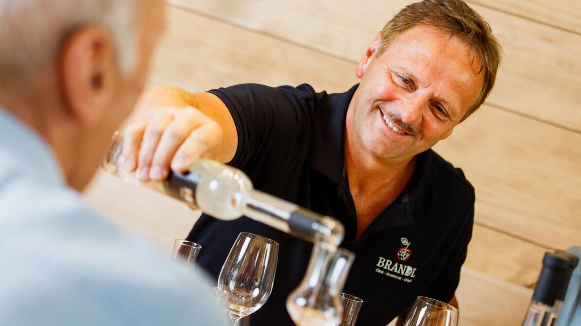 Ein Kellner schenkt Wein in ein Glas für einen Gast. Beide Männer lächeln und genießen die Atmosphäre. | © Familie Brandl