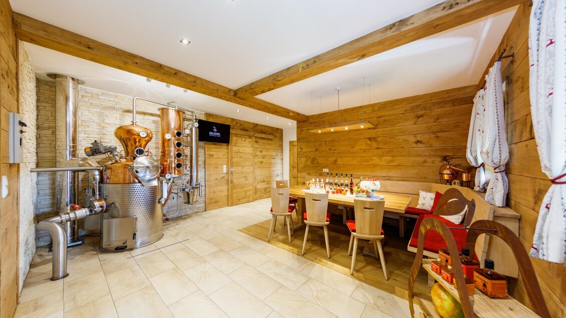 Ein stilvolles, rustikales Zimmer mit Holzwänden und einem großen Tisch. Eine Destillieranlage steht an der Wand, die den ländlichen Charme ergänzt. | © Familie Brandl